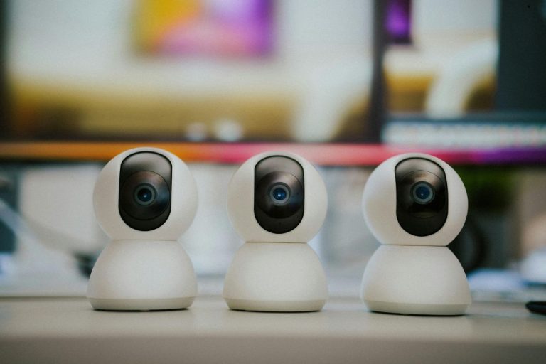 A desk featuring three small white wireless security cameras placed in front of a computer, ideal for monitoring.