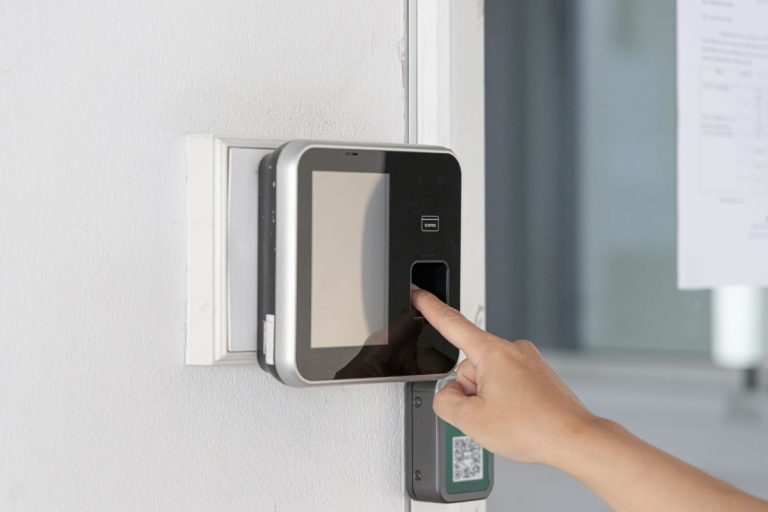 A person using a biometric scanner on a wall to gain access, with a card reader visible below the touchscreen device.